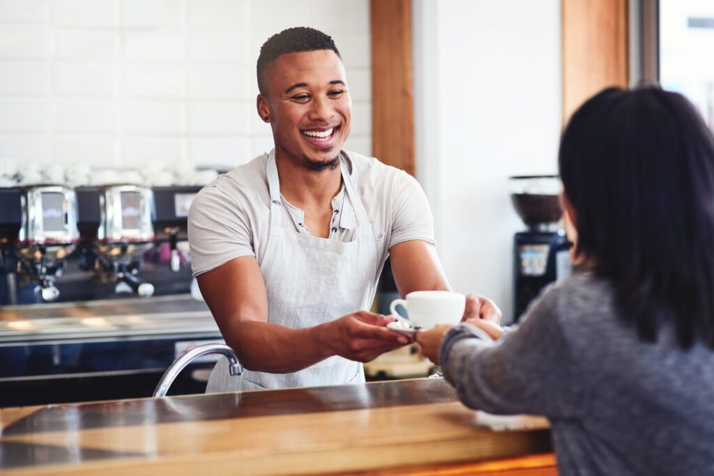 Shot of a young barista serving a cup of coffee to a customer in a cafe representing your coffee service staff